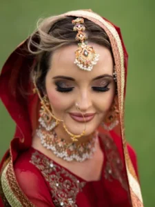 Blonde bride adorned in traditional Indian bridal makeup, featuring intricate jewelry and a draped dupatta, created by Fouzia Rana of Labelle Hair and Makeup in Brampton, showcasing mobile/on-site services across the Greater Toronto Area.