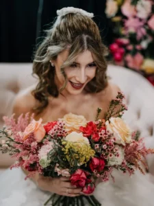 Blonde bride hair Balayage and ethnic makeup glow holding flowers in her hand.