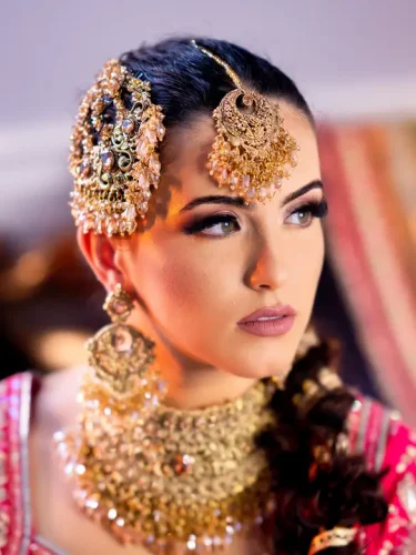 Close-up of a South Asian bride with detailed golden jewelry and elaborate hairstyle, showcasing cultural beauty.