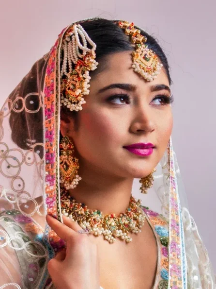 Bride with colorful jewelry looking upwards, wearing bright pink lipstick.