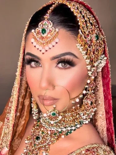South Asian bride in a sheer veil with gold and pearl jewelry, looking pensive.