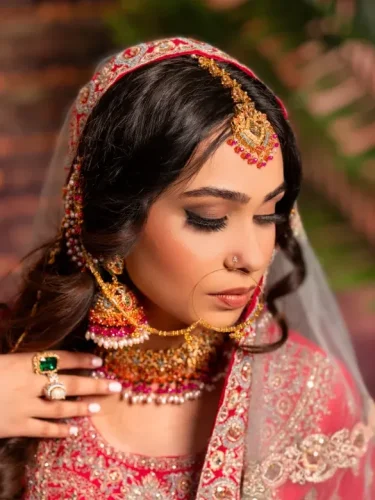 South Asian bride in red with intricate gold jewelry, gently touching her chin.