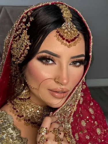 South Asian bride in a red veil with heavy gold jewelry, looking serene.