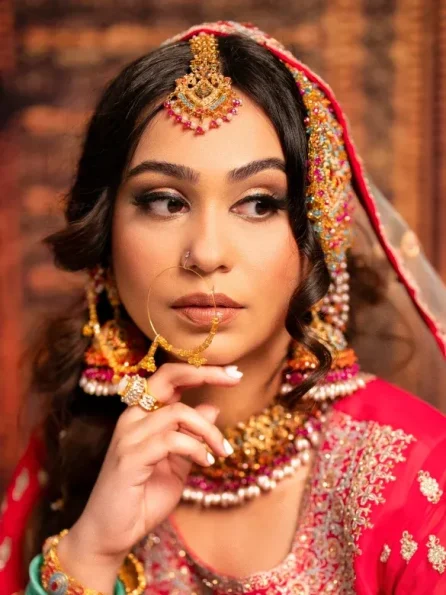 Close-up of a bride in a red outfit with detailed gold jewelry, looking away thoughtfully.