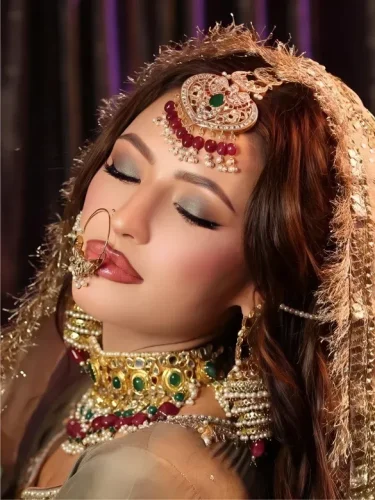 South Asian bride with ruby and emerald jewelry, and a contemplative gaze.